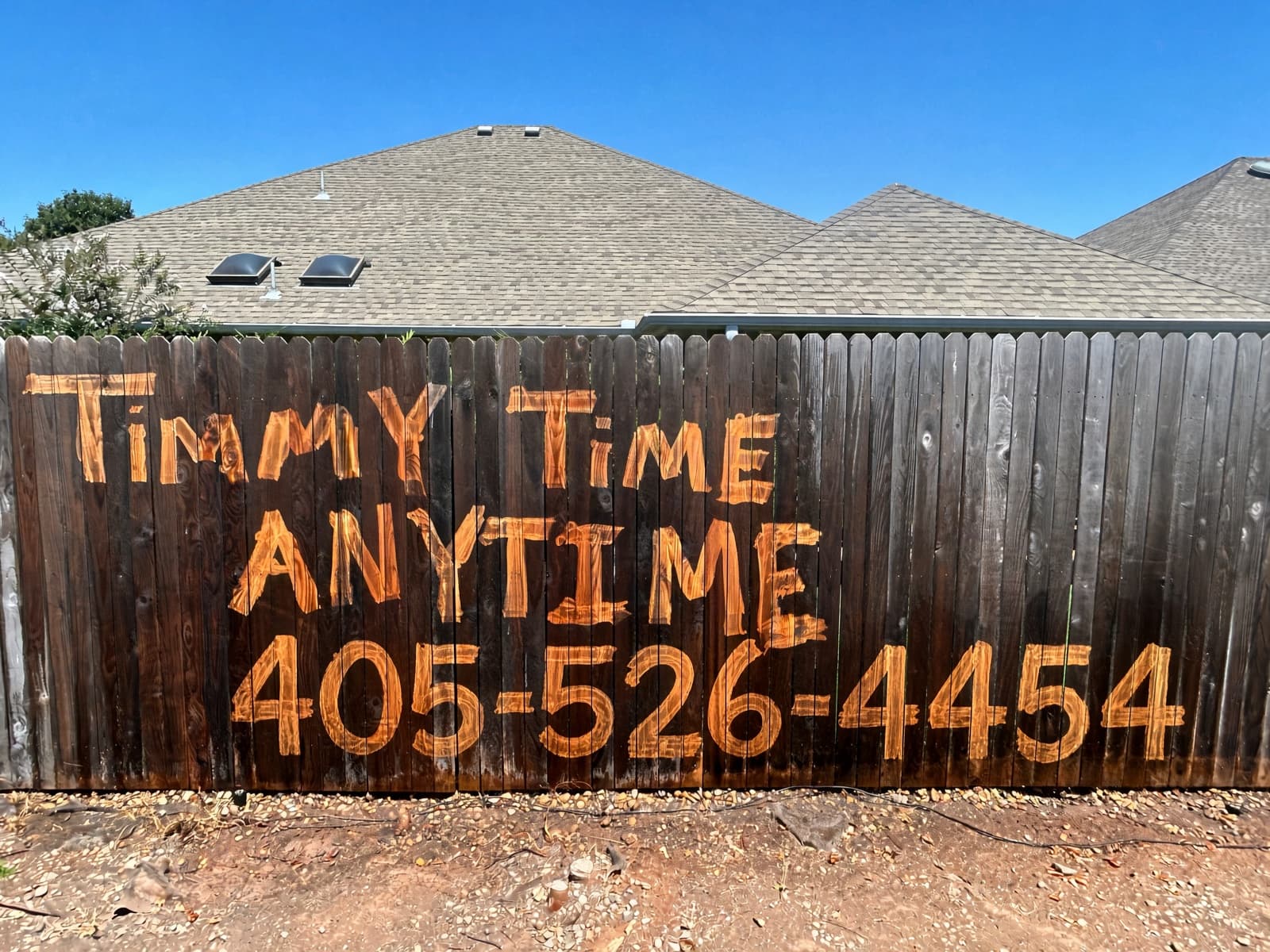 Power-washed wood fence with Timmy Time Anytime painted on the boards.
