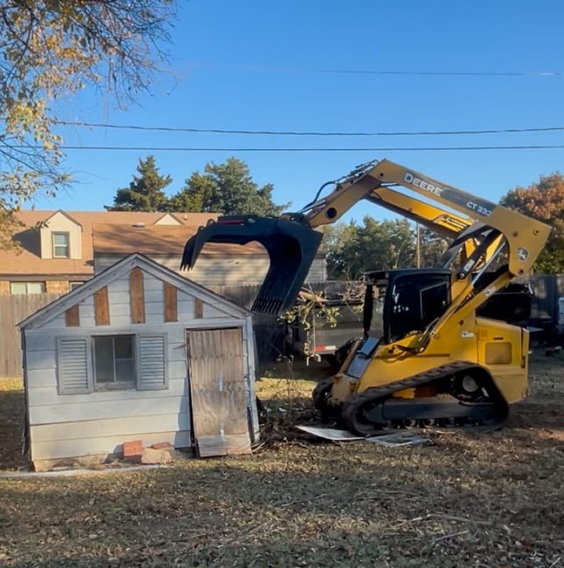 A track loader tearing down an old backyard shed.