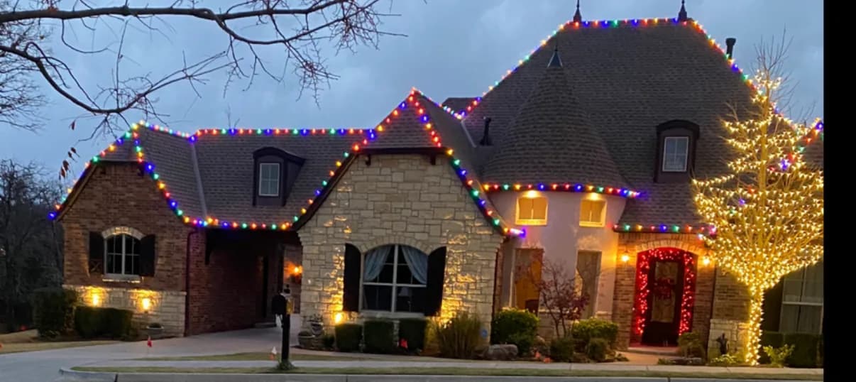 Christmas lights on a stone house at dusk.